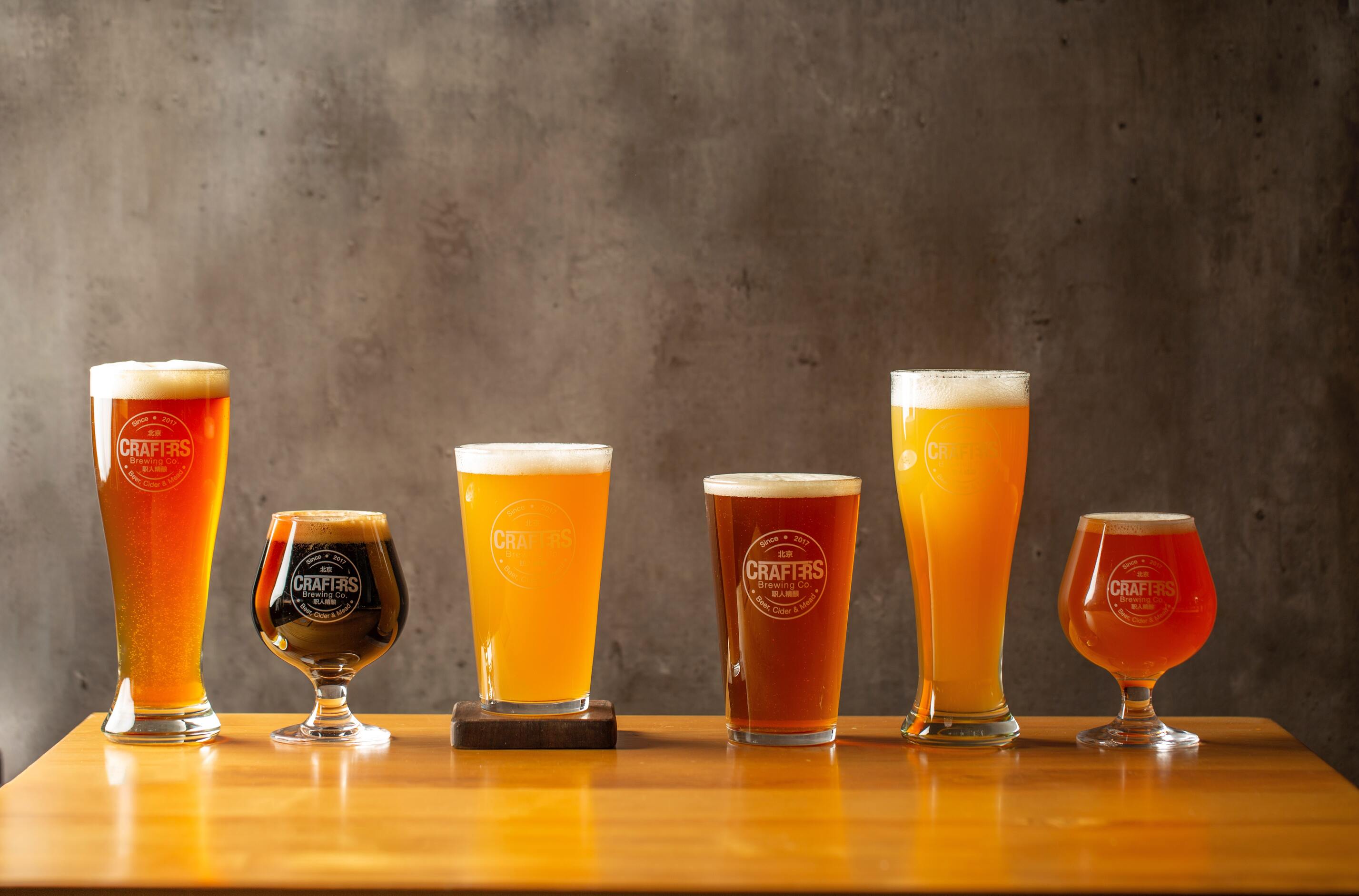 Six glasses of light, medium, and dark craft beers in specialty glasses