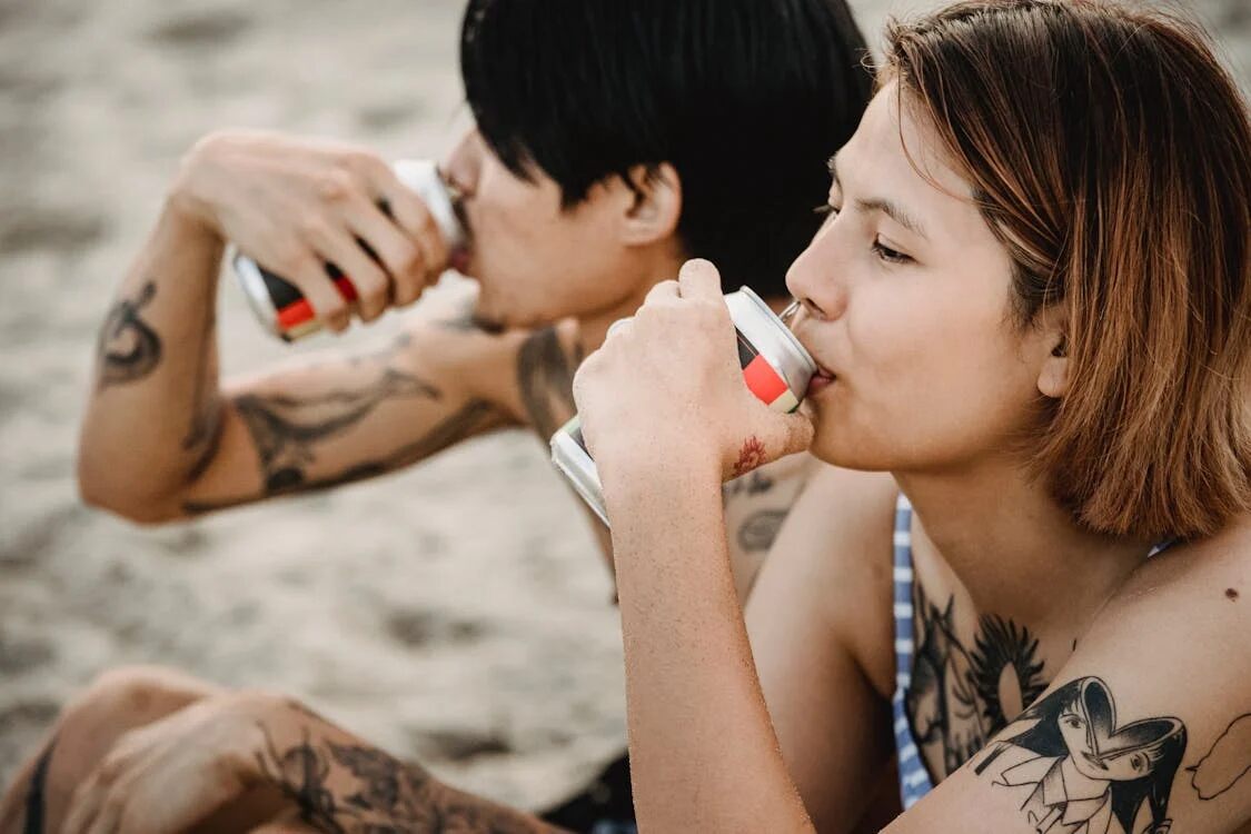 Woman and man drinking from cans at beach