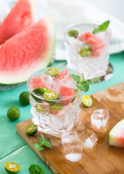 A watermelon cocktail flat lay with ice, watermelon, and key limes