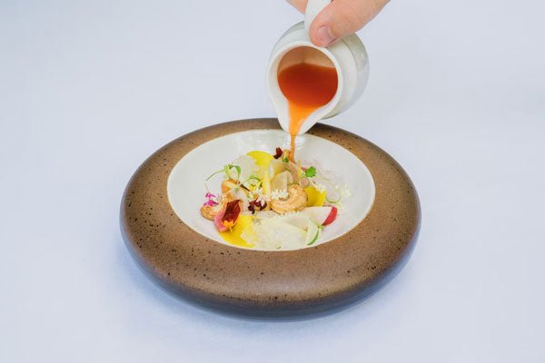 A chef pouring a fruit puree sauce on a dish