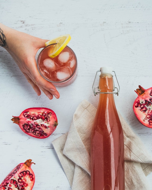 A jar of fermenting kombucha pomegranates and a hand grabbing an ice cold glass